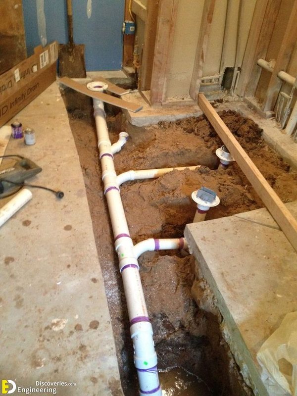White PVC drain pipes laid in an excavated trench in a concrete slab